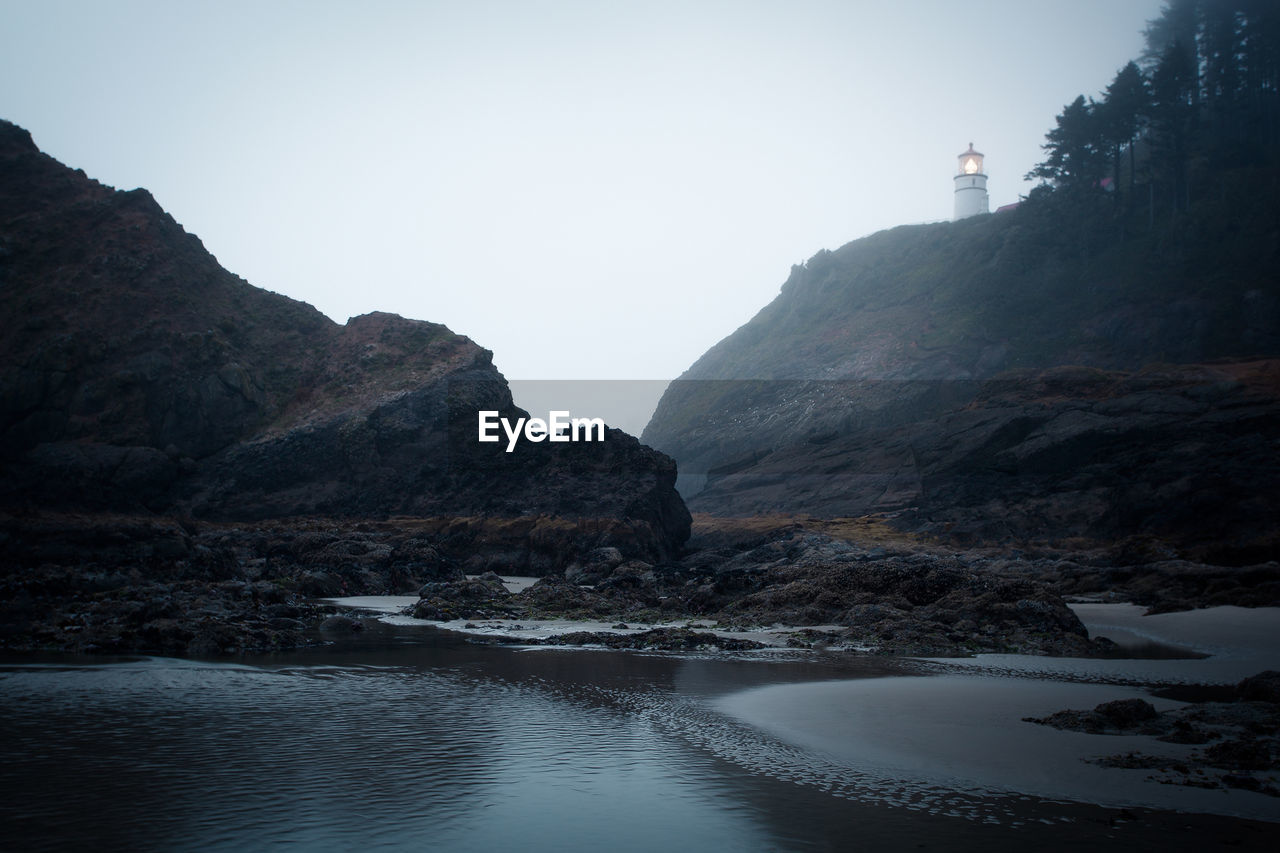 Lighthouse on cliff by sea against sky