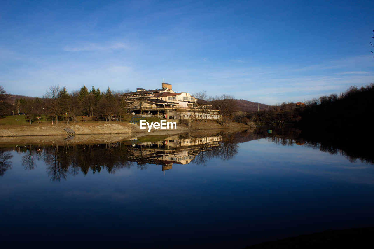 Buildings by lake against blue sky