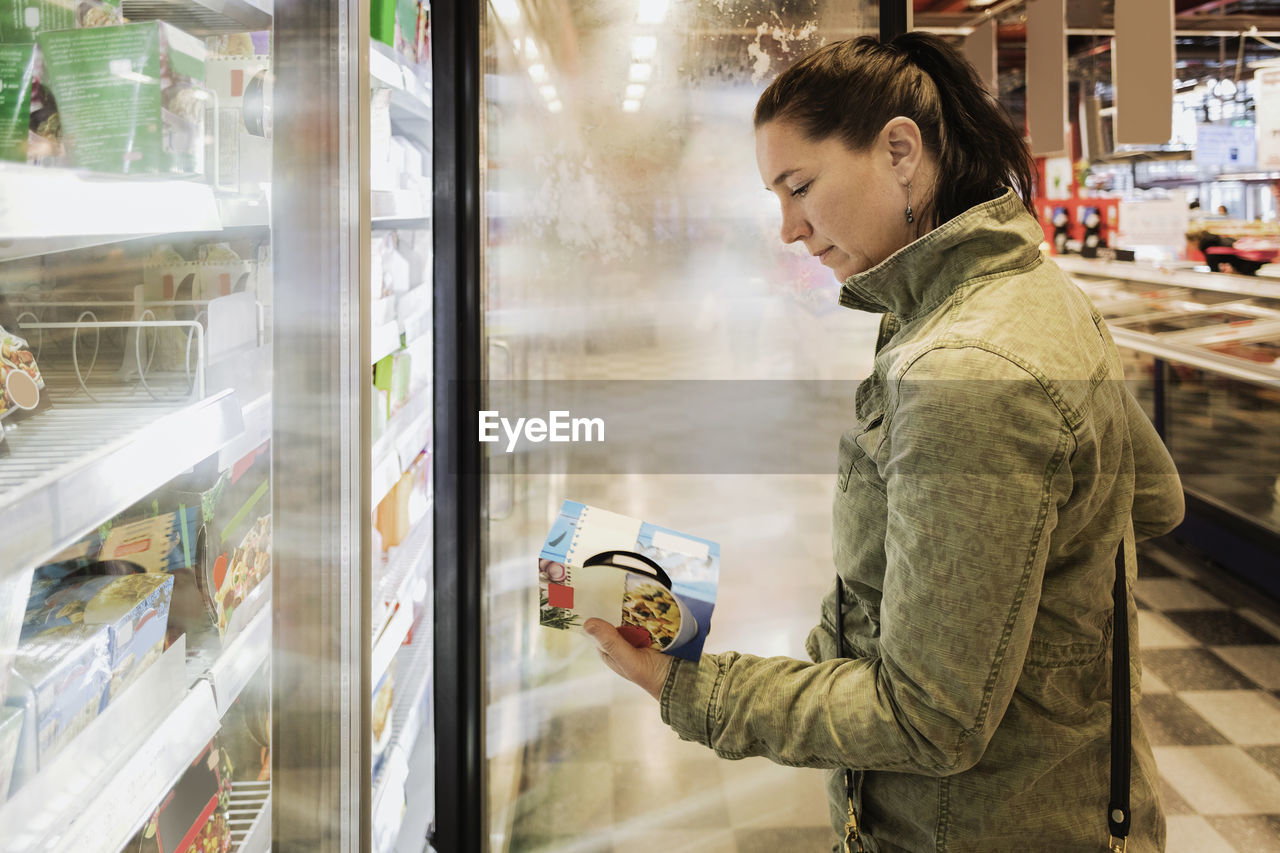 Side view of woman reading food label at refrigerated section