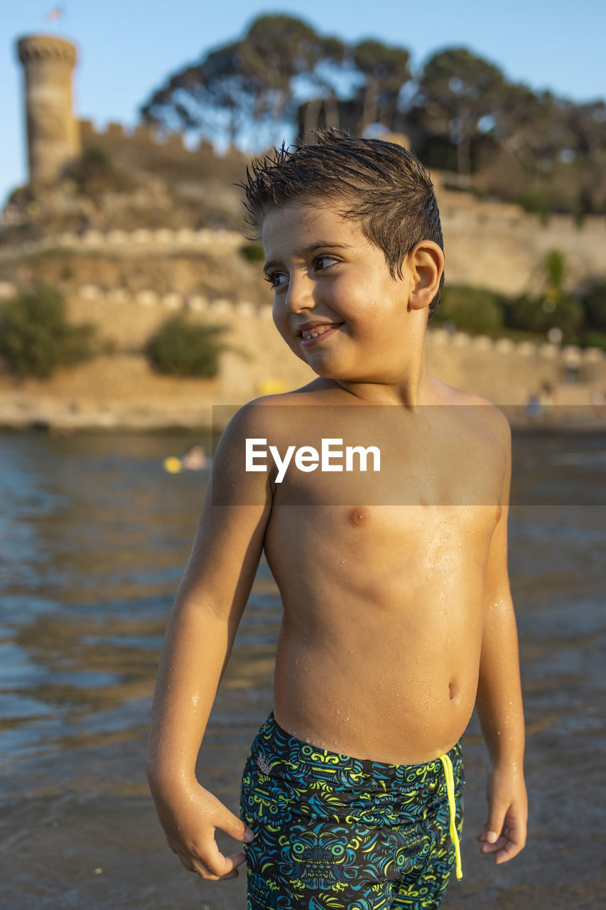 Shirtless boy standing by water outdoors