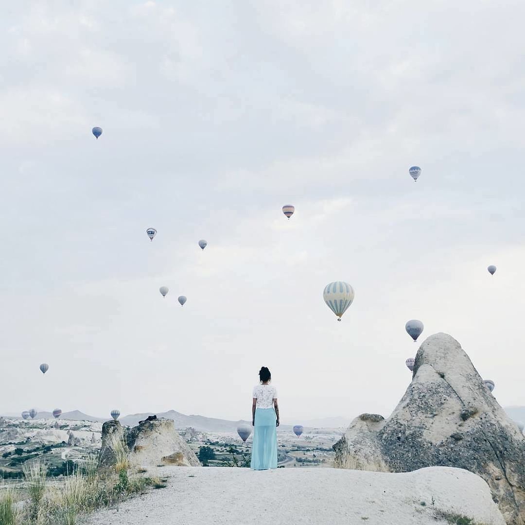 Rear view of woman standing against hot air balloons in sky at cappadocia