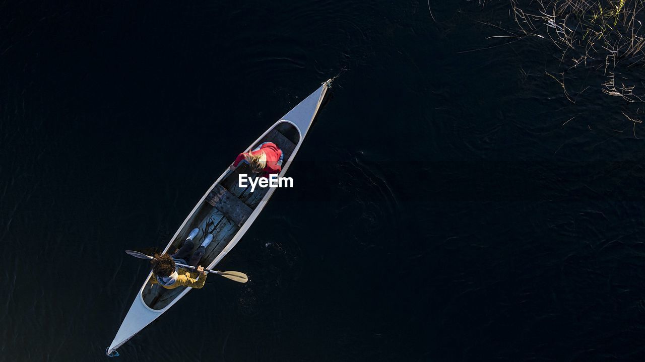 Young man paddling through oar while sitting with woman in canoe on river during sunset