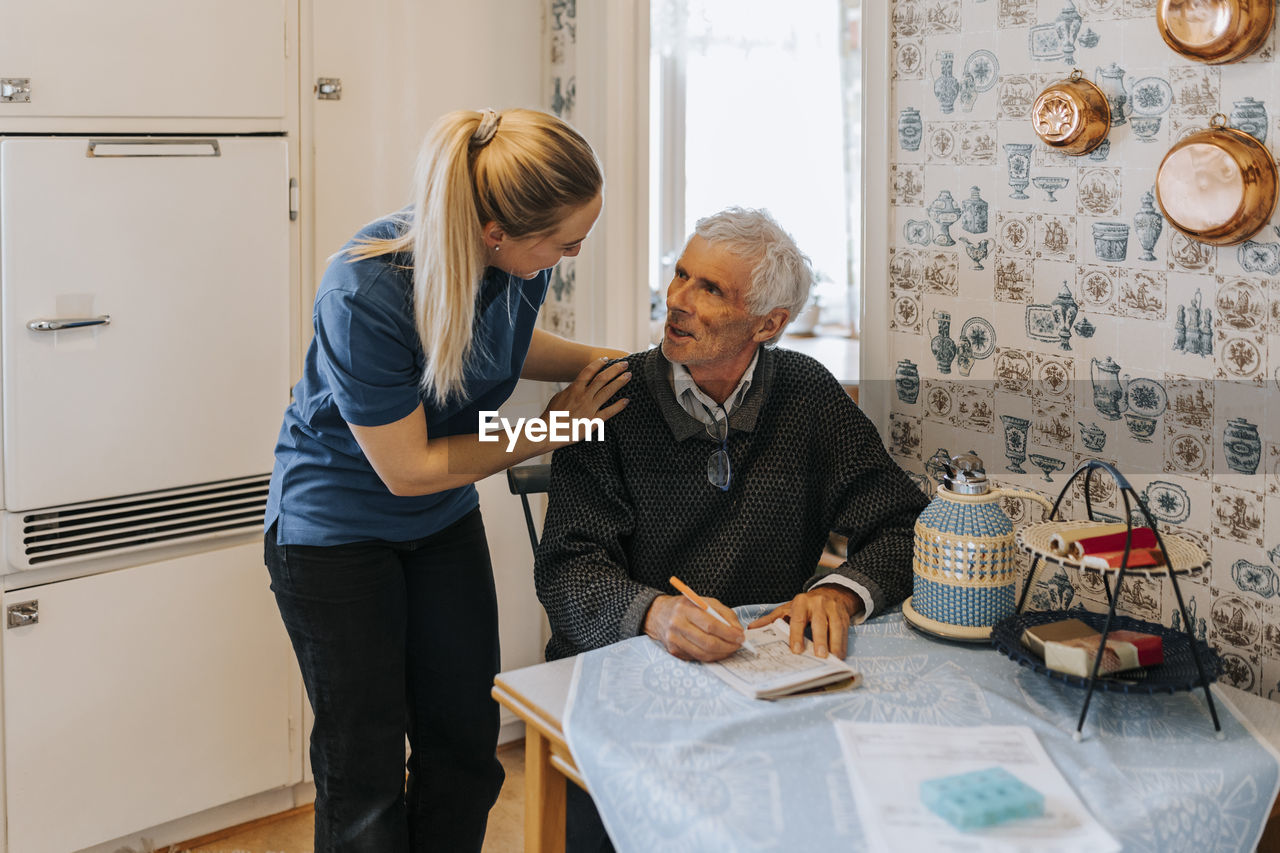 Female care assistant talking to senior man doing soduko at home