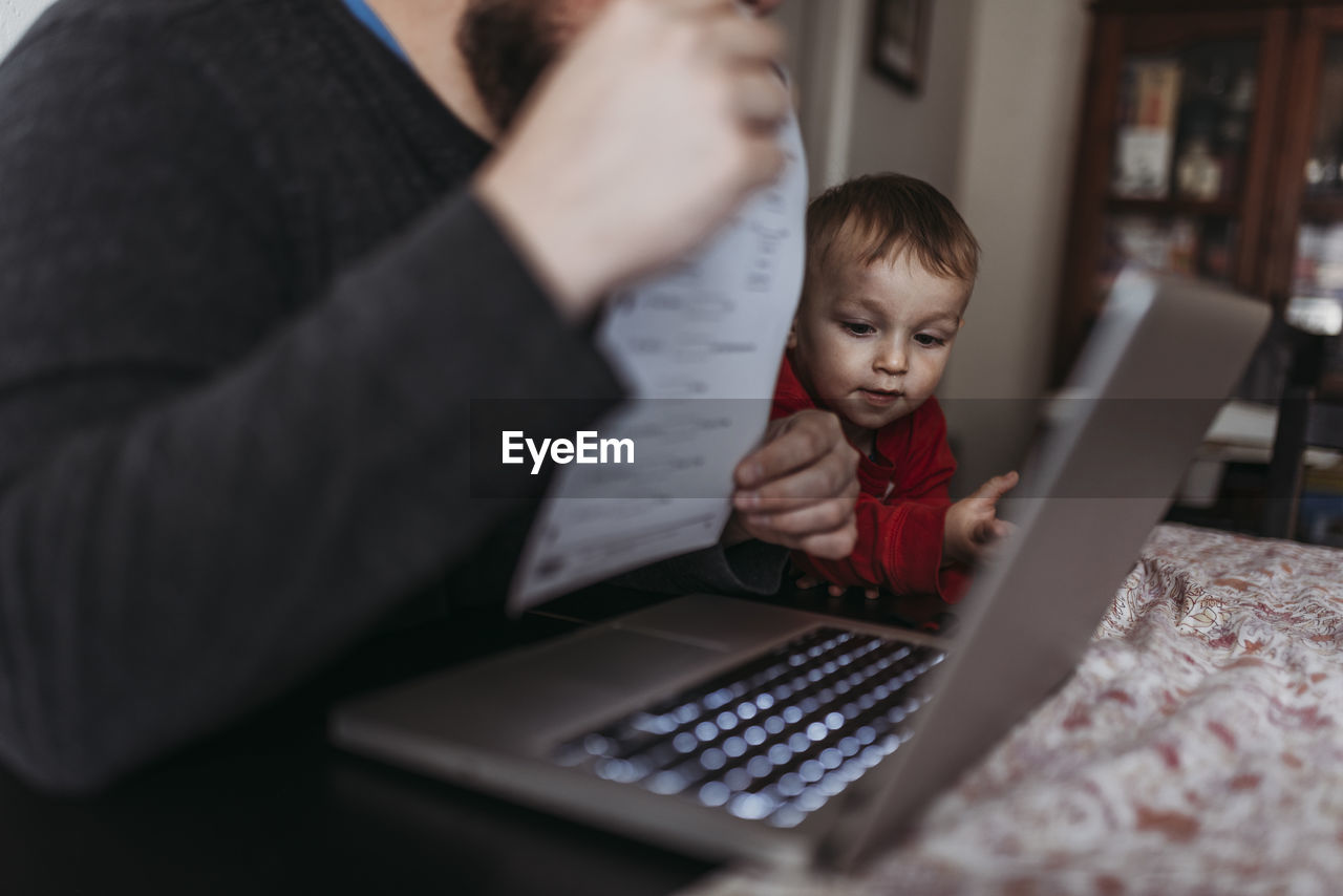 Close up of young son looking at dads computer while he works at home