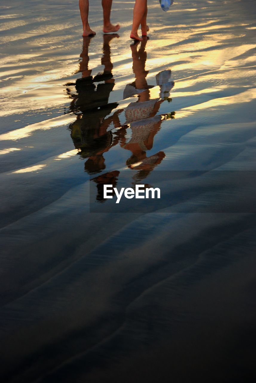 Low section of man and woman reflecting while walking at beach