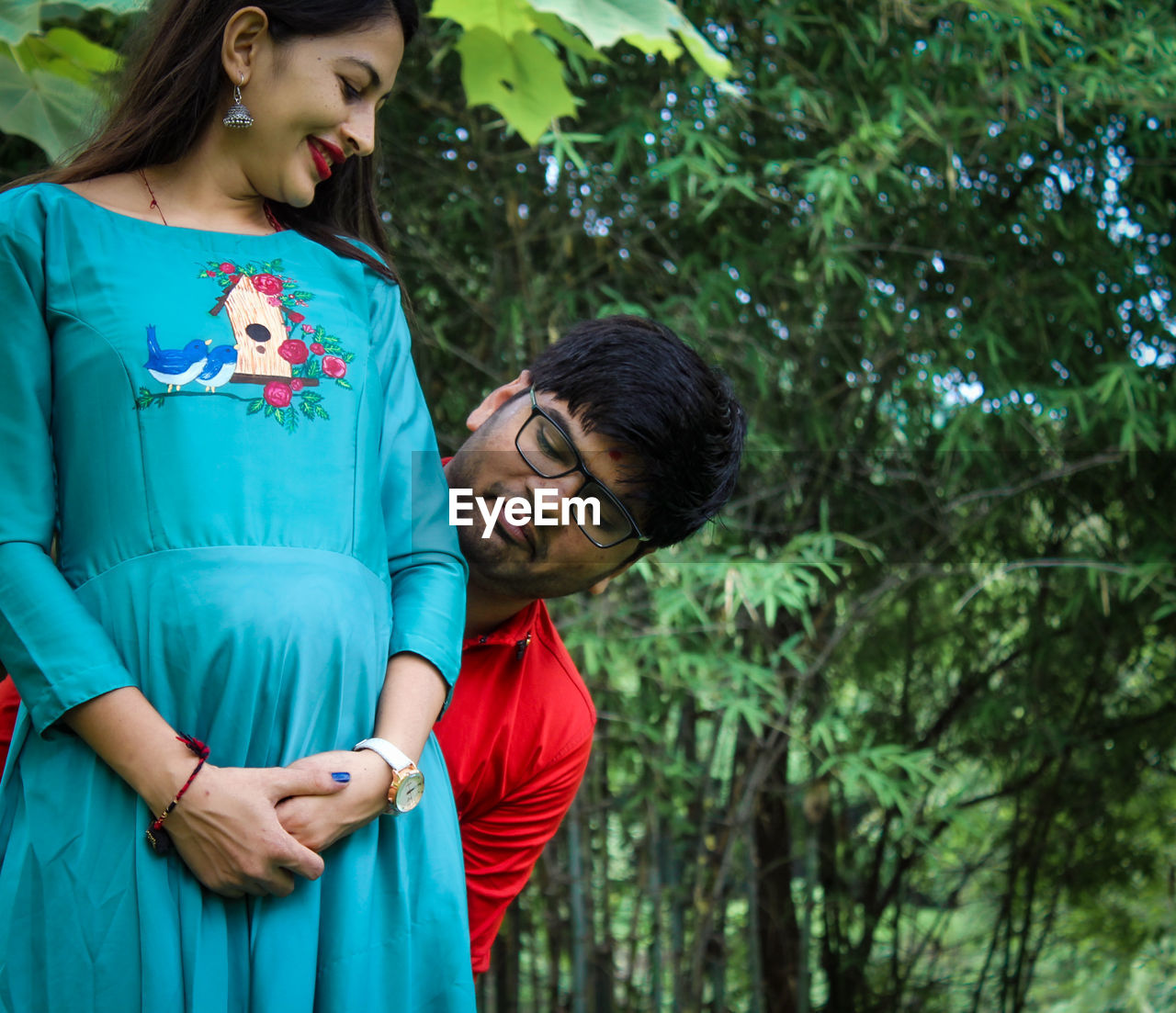 Man looking at pregnant woman abdomen against tress in forest