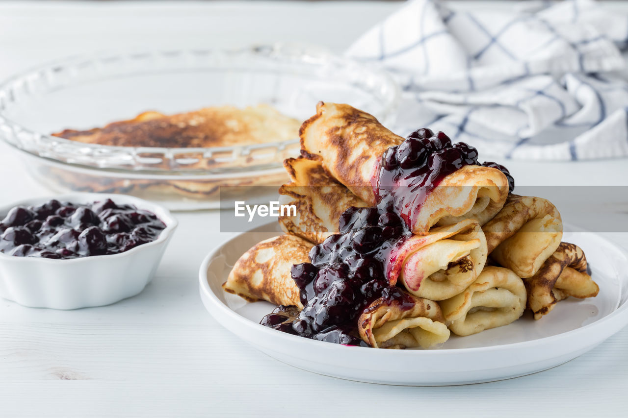 A pile of delicious rolled crepes topped with homemade blueberry sauce.