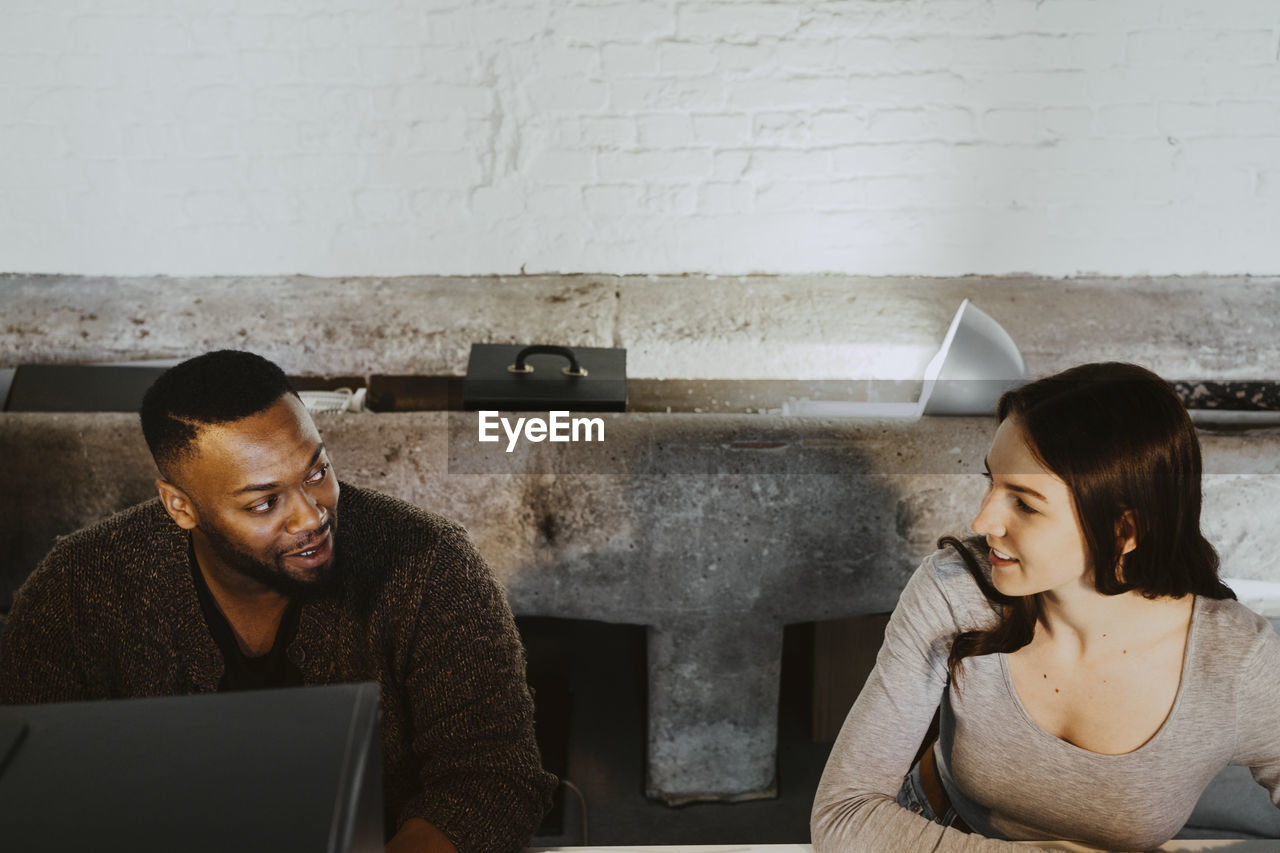 Female and male programmers talking while working on computer in creative office