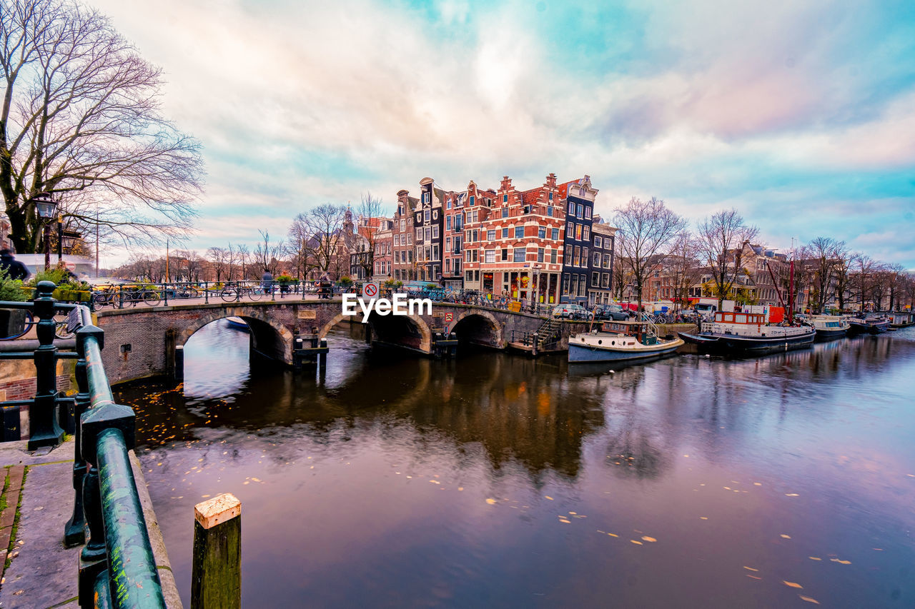 BRIDGE OVER RIVER AMIDST BUILDINGS AGAINST SKY