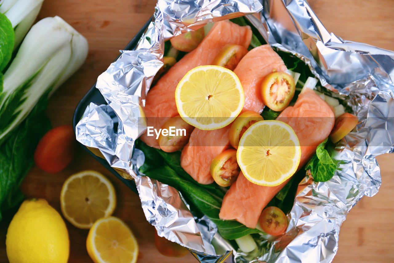 High angle view of meat and lemon in foil on table