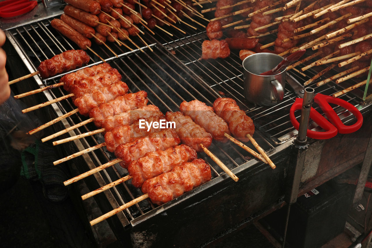 meat, barbecue, food, grilling, food and drink, barbecue grill, grilled, freshness, heat, cooking, outdoor grill, dish, fast food, cuisine, skewer, sausage, high angle view, preparing food, hand, red meat, burning, arrosticini, roasting, metal, serving tongs, outdoors, coal, fire, street food, smoke, yakiniku, grid, day, kebab