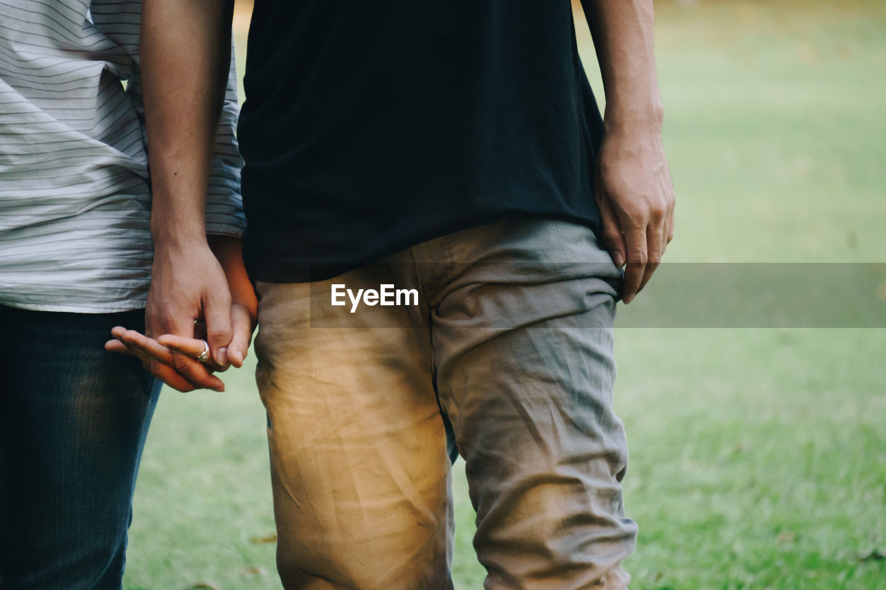 Midsection of couple holding hands while standing in park