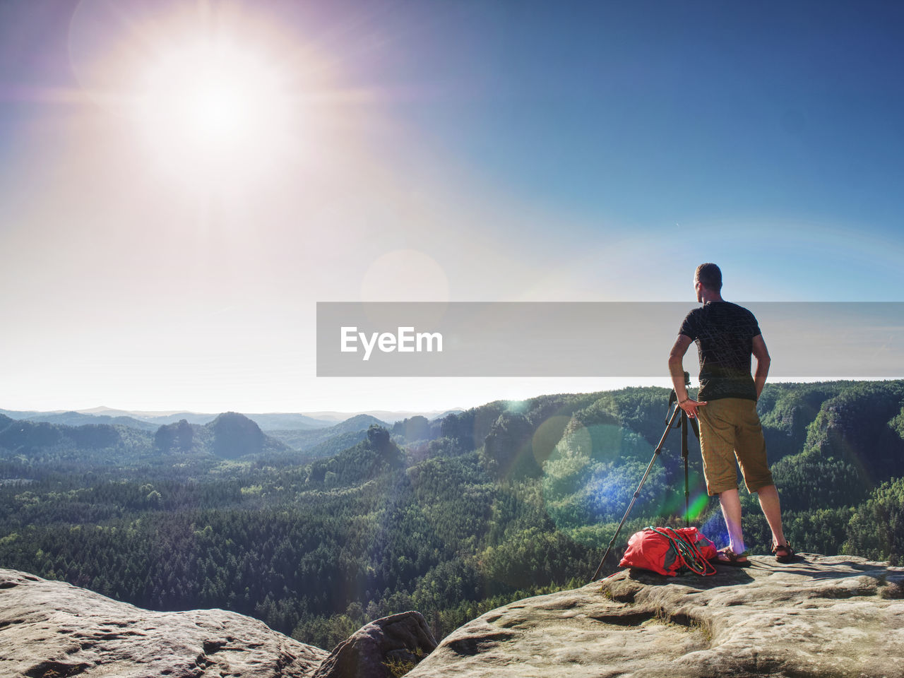 REAR VIEW OF MAN STANDING BY MOUNTAIN AGAINST SKY