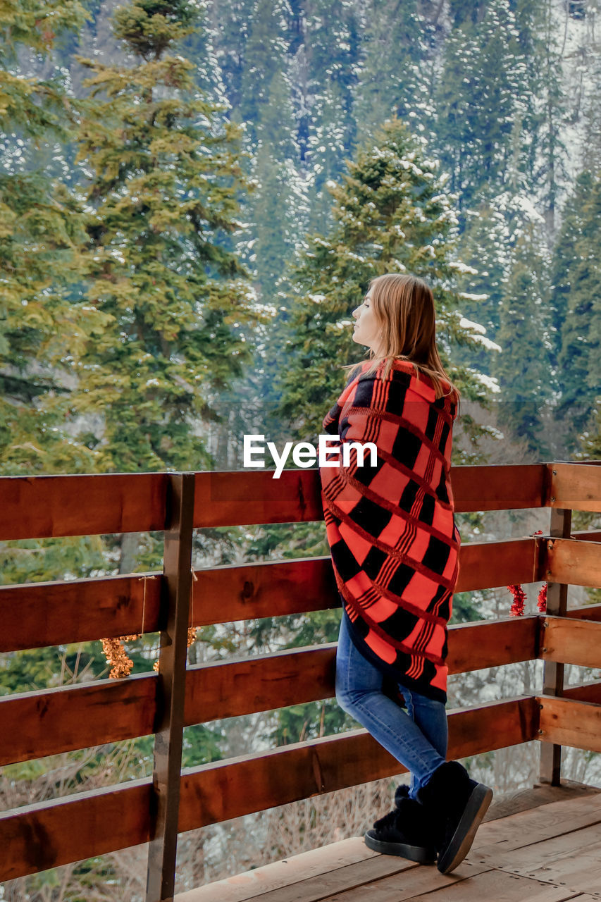 Woman standing by railing against trees