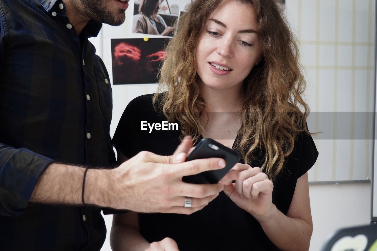 Man showing mobile phone to female colleague in office