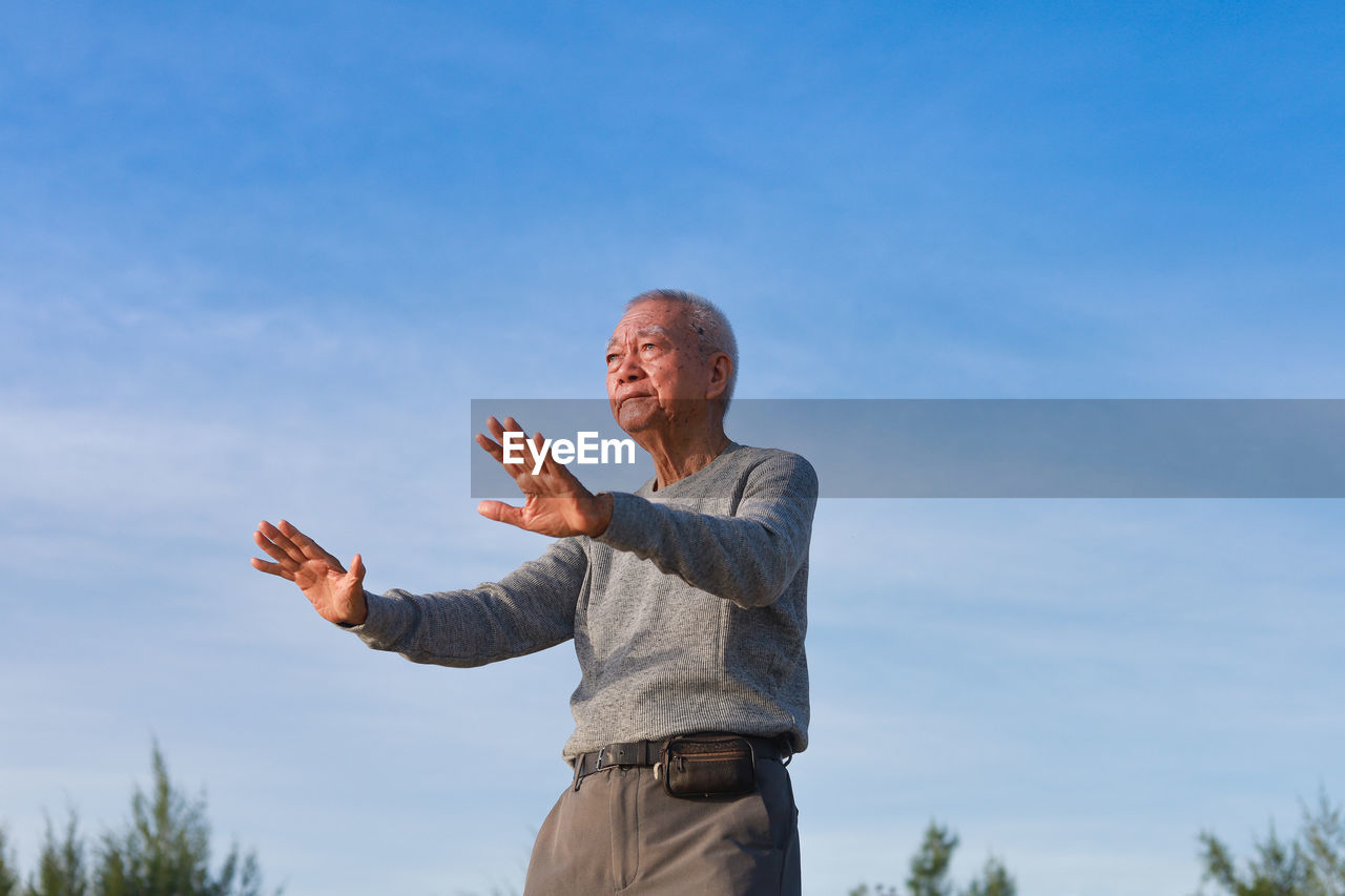 Low angle view of senior man exercising against blue sky