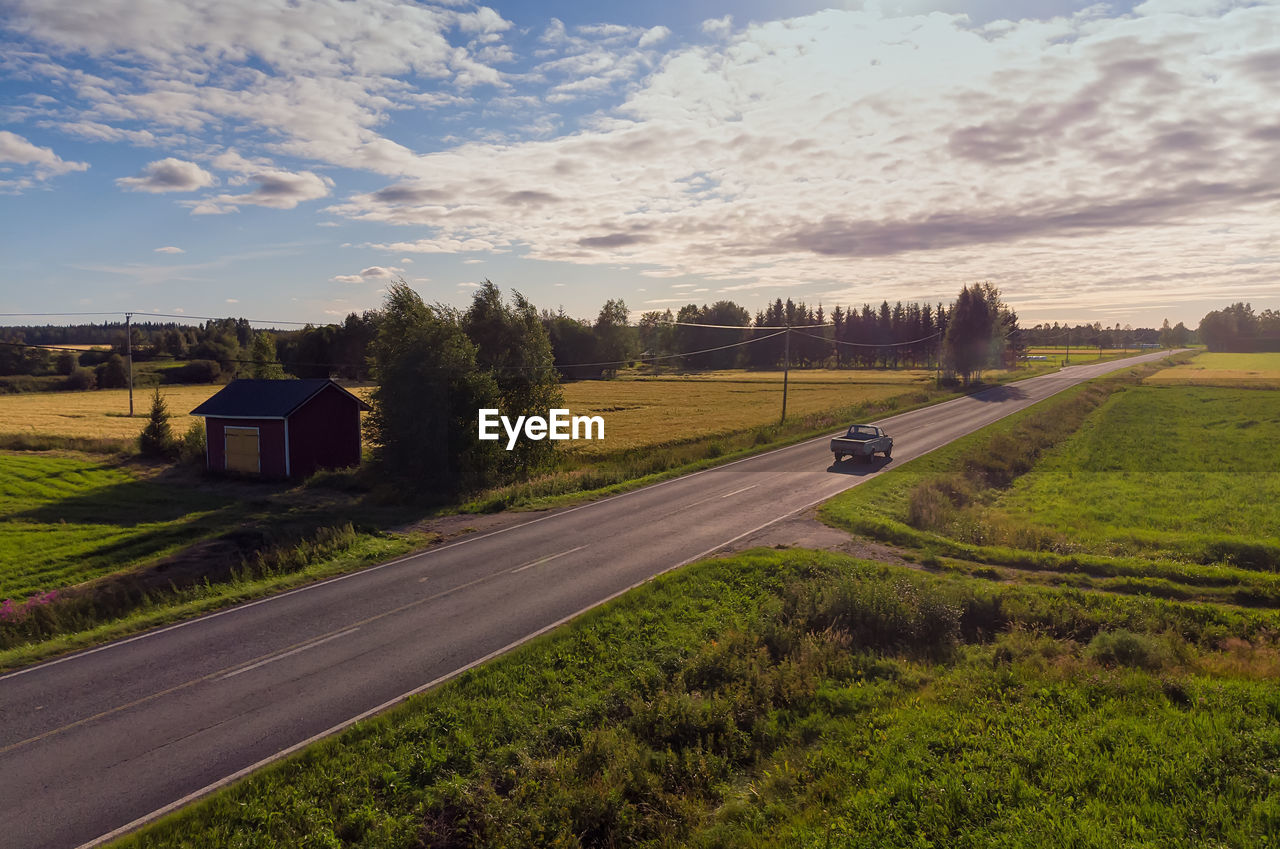 A pickup truck drives on a country road on a beautiful summer evening at the rural finland.