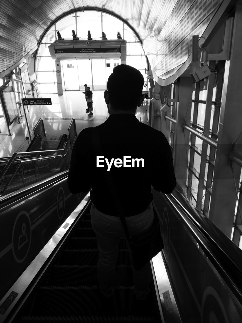 REAR VIEW OF MAN STANDING AT ESCALATOR