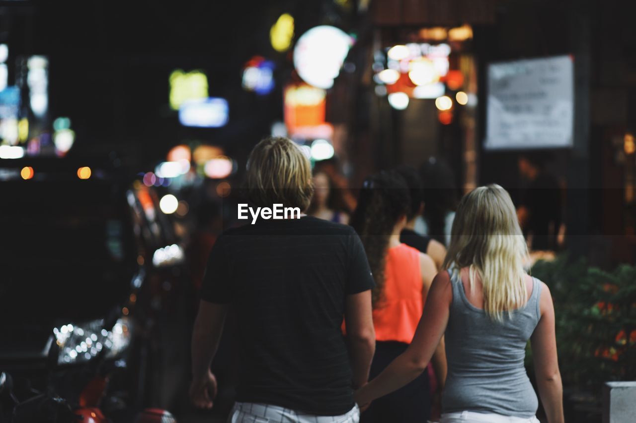 Rear view of people walking on city street at night