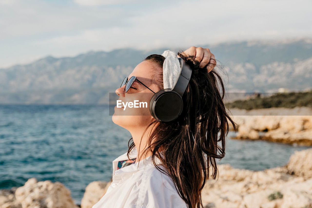 Side view of young woman in white shirt listening to music on headphones. summer, beach, lifestyle.