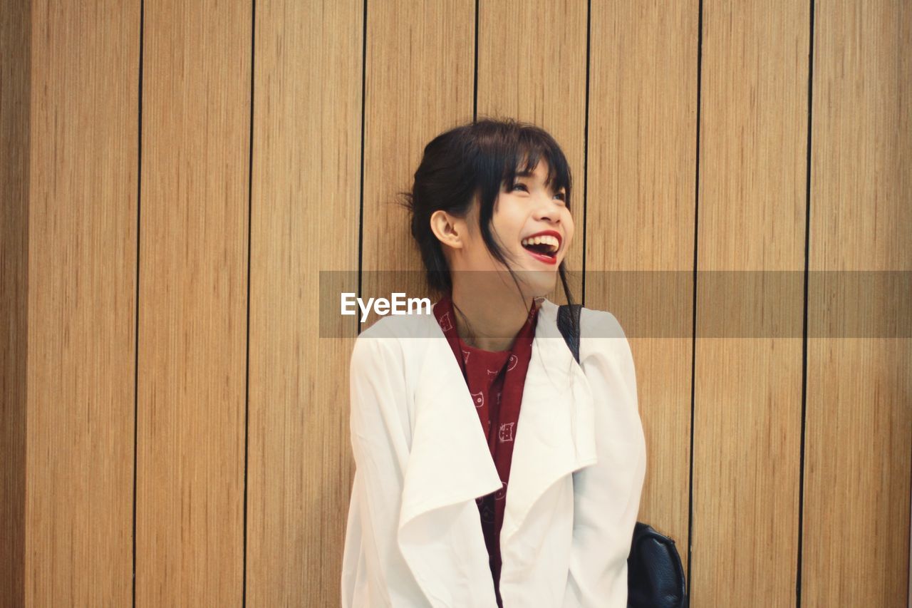 Young woman laughing against wooden wall