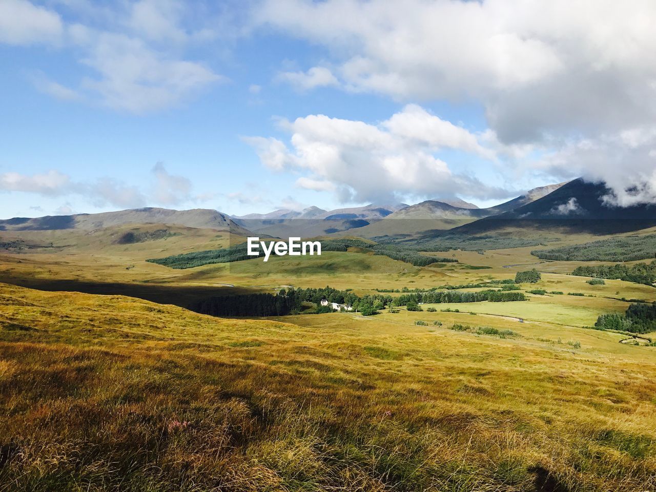 Scenic view of green landscape and mountains against cloudy sky