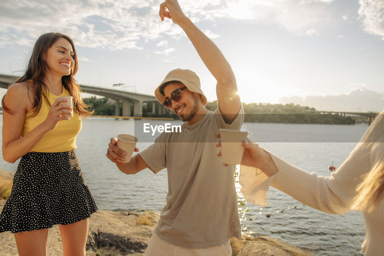 Carefree young man dancing with hand raised by female friends during picnic