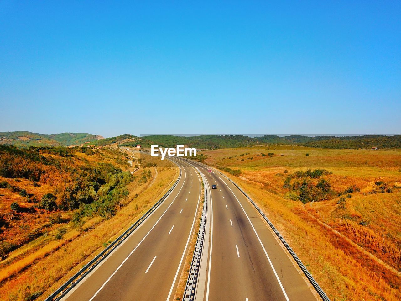 Road passing through landscape against clear blue sky