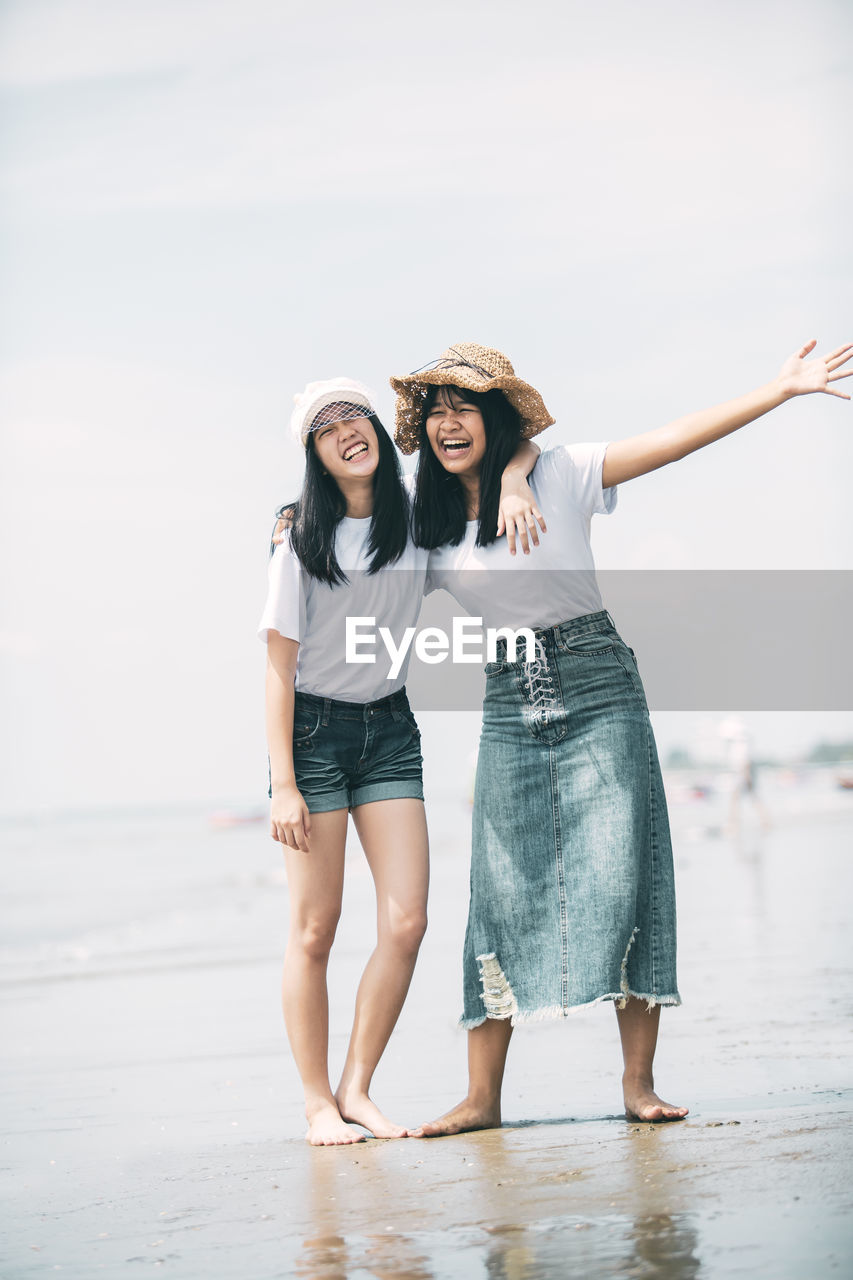 Full length of girls standing at beach against sky