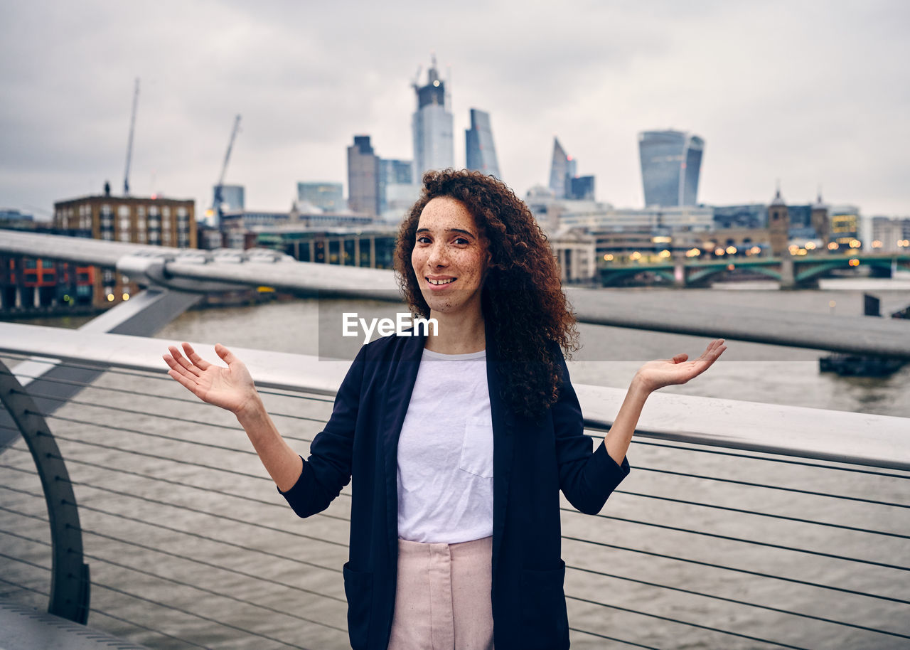 Portrait of woman gesturing while standing against thames river in city