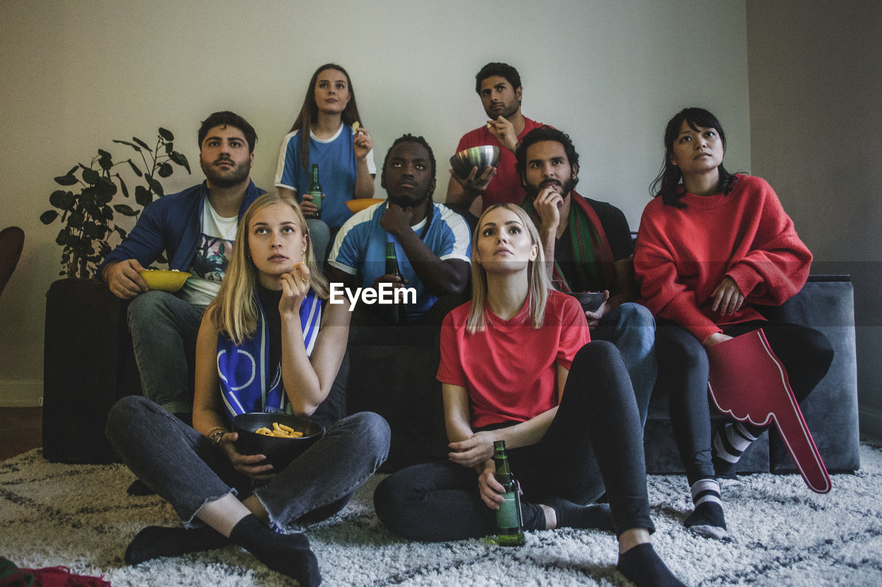 Male and female fans watching soccer match while sitting at home