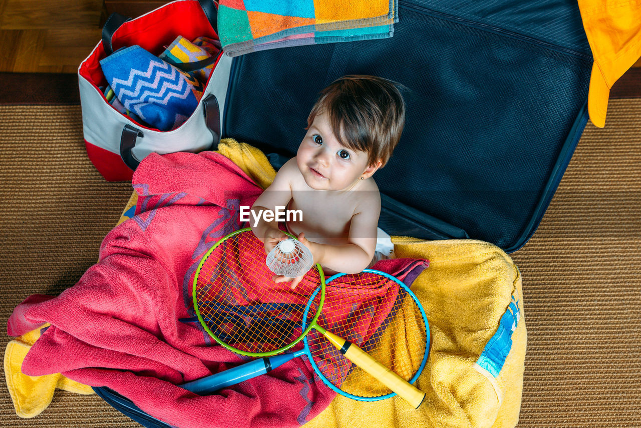 High angle portrait of boy holding shuttlecock while sitting in suitcase