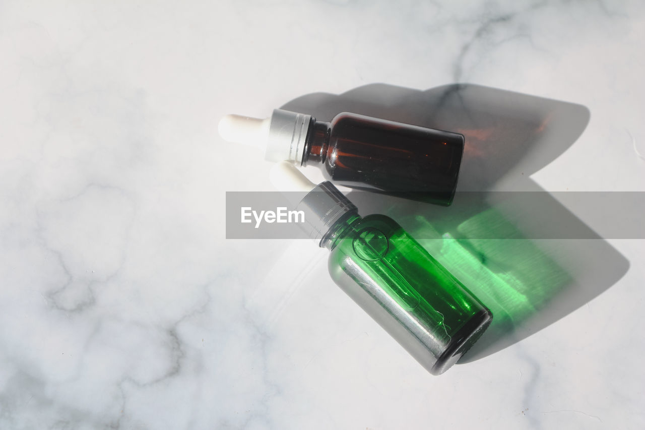 Green and brown bottle facial essential oil or serum packaging on white marble background. 