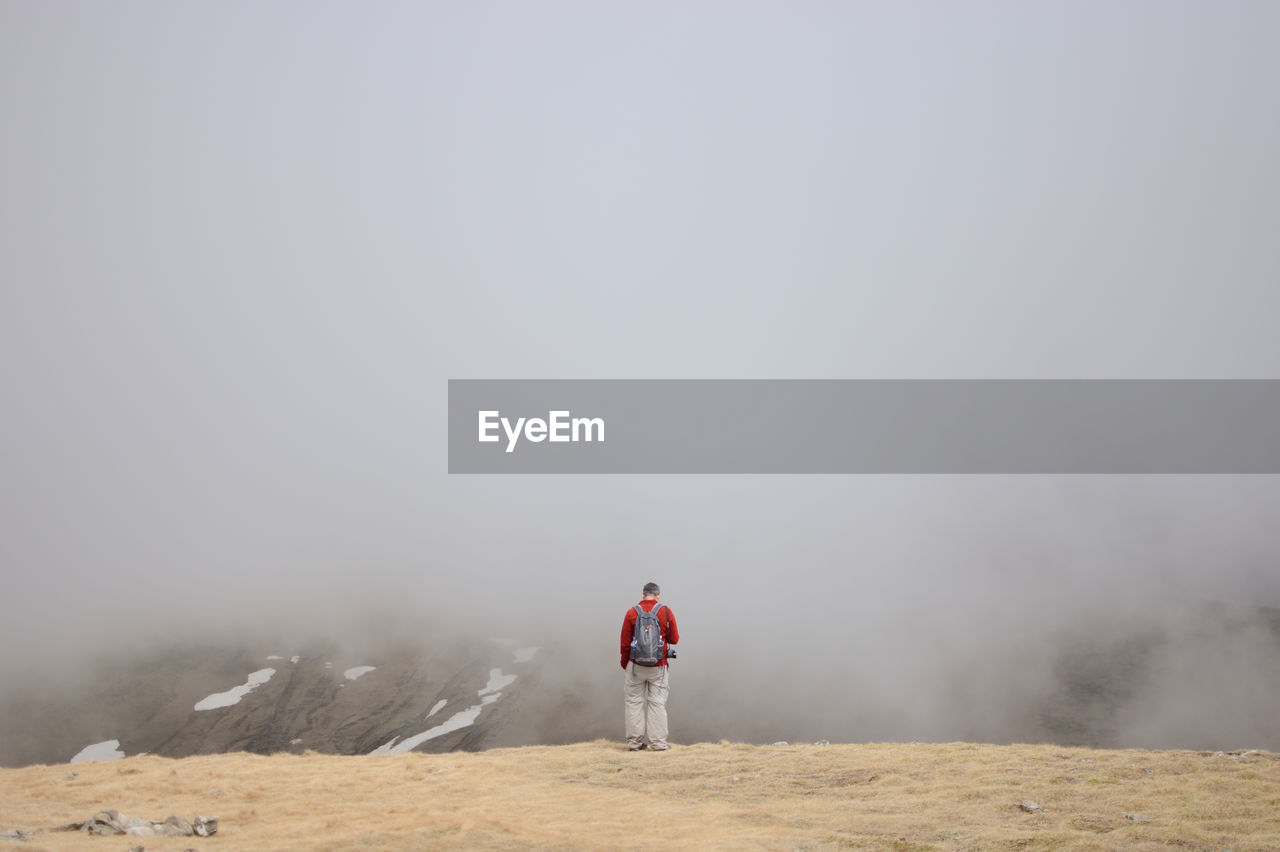 Rear view of man standing on landscape against sky