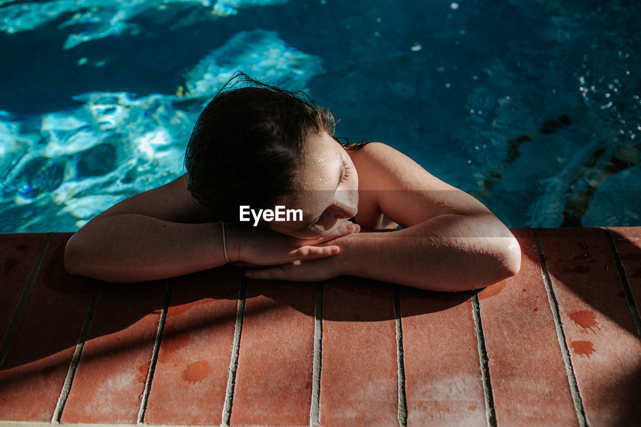 Tween girl resting head on the side of a swimming pool