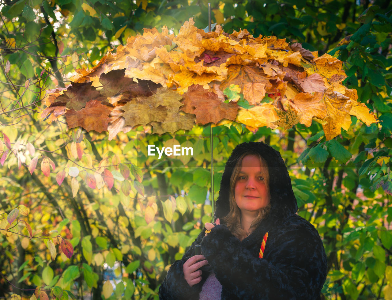 Female model holds an umbrella with autumn leaves on it in hand to the autumn beginning