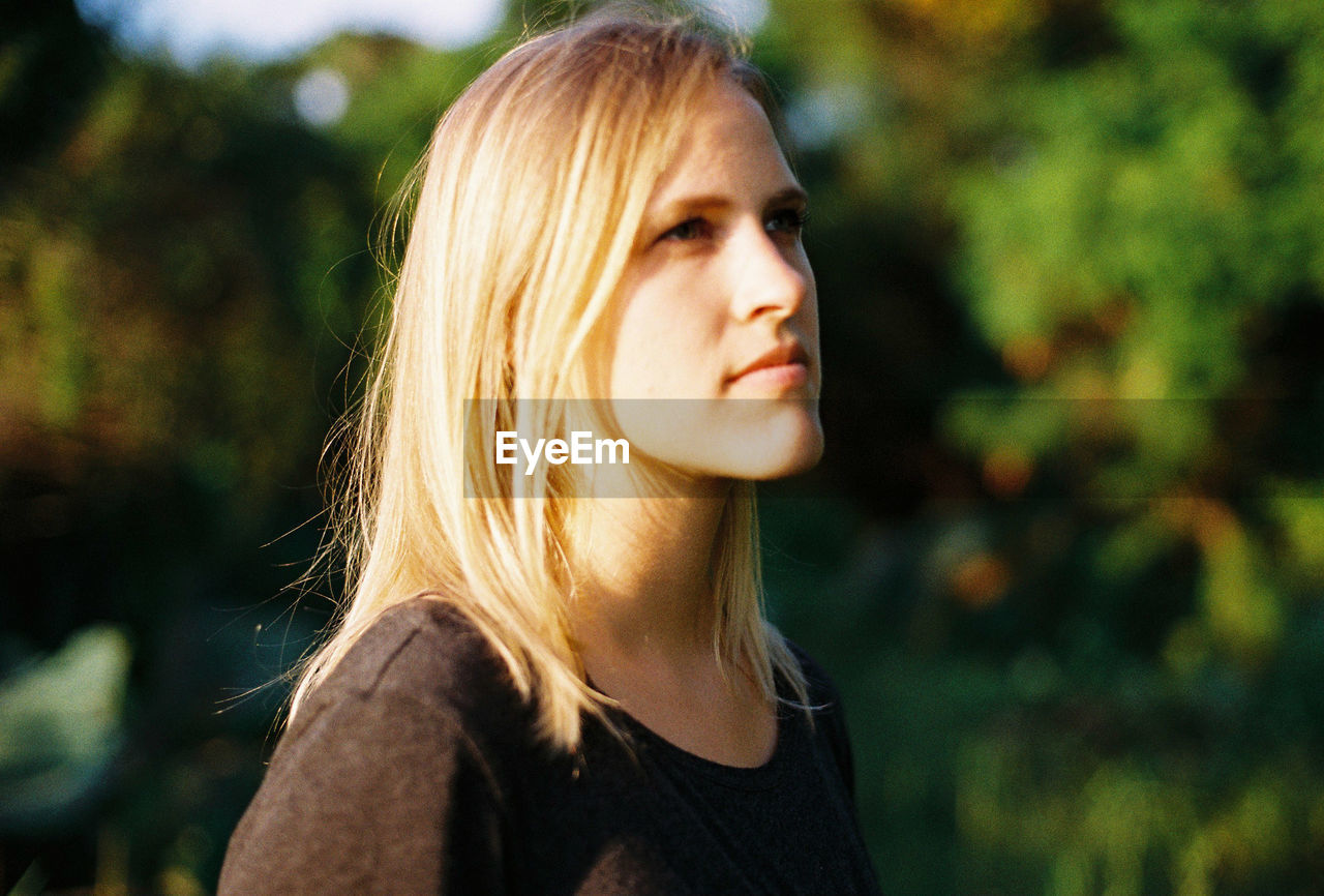 Young woman looking away against trees