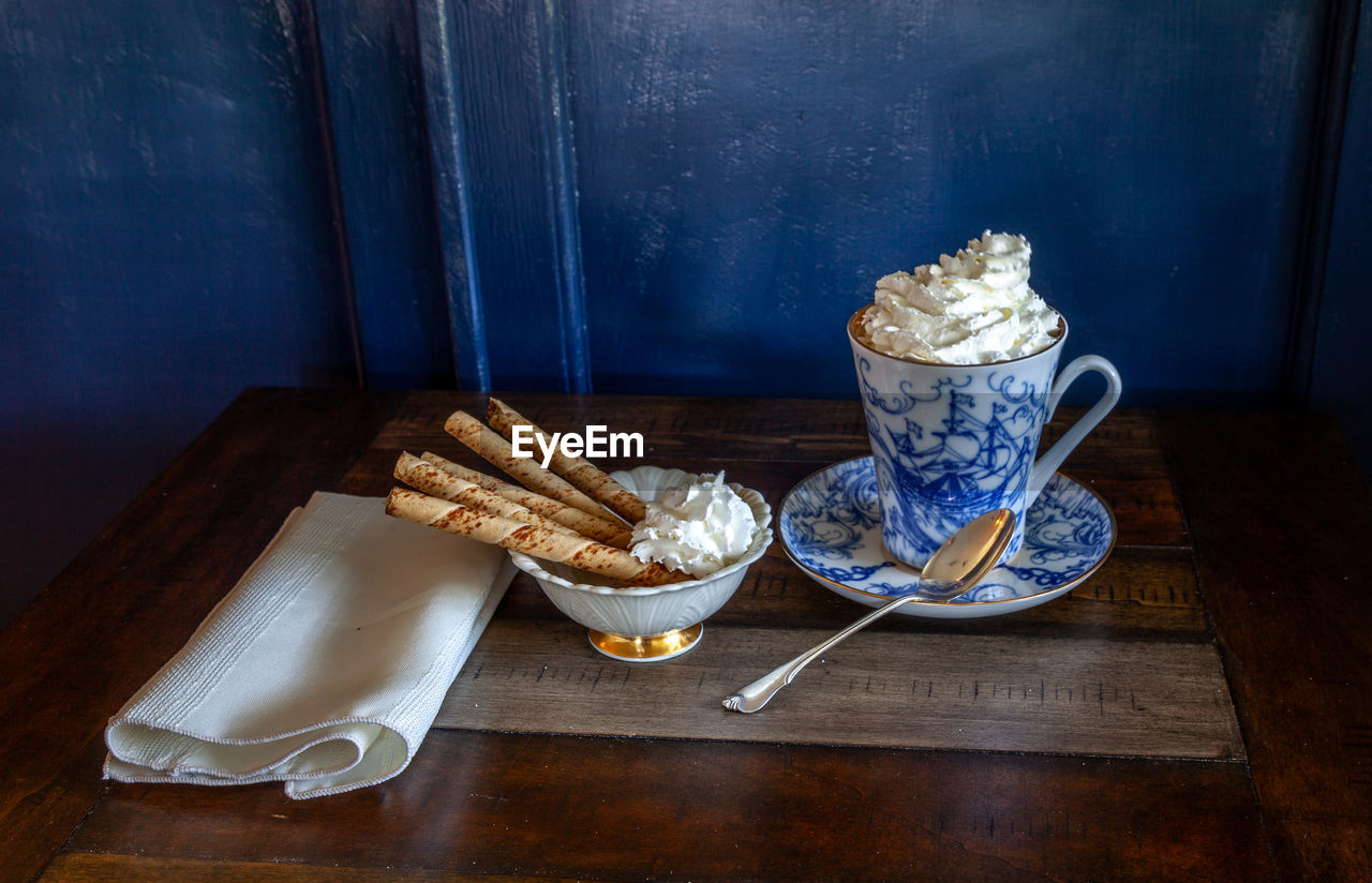 Gourmet hot chocolate and whip cream in a nautical china mug with cookies on a rustic table