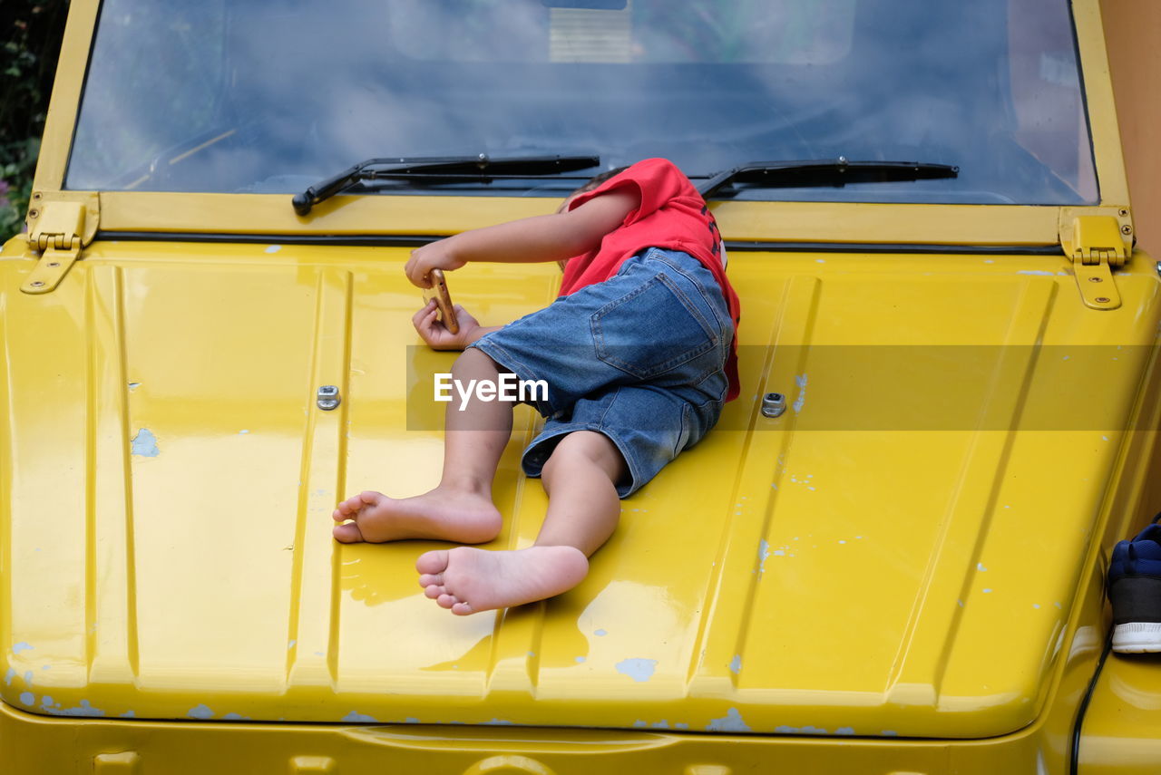 REAR VIEW OF BOY LYING ON YELLOW CAR