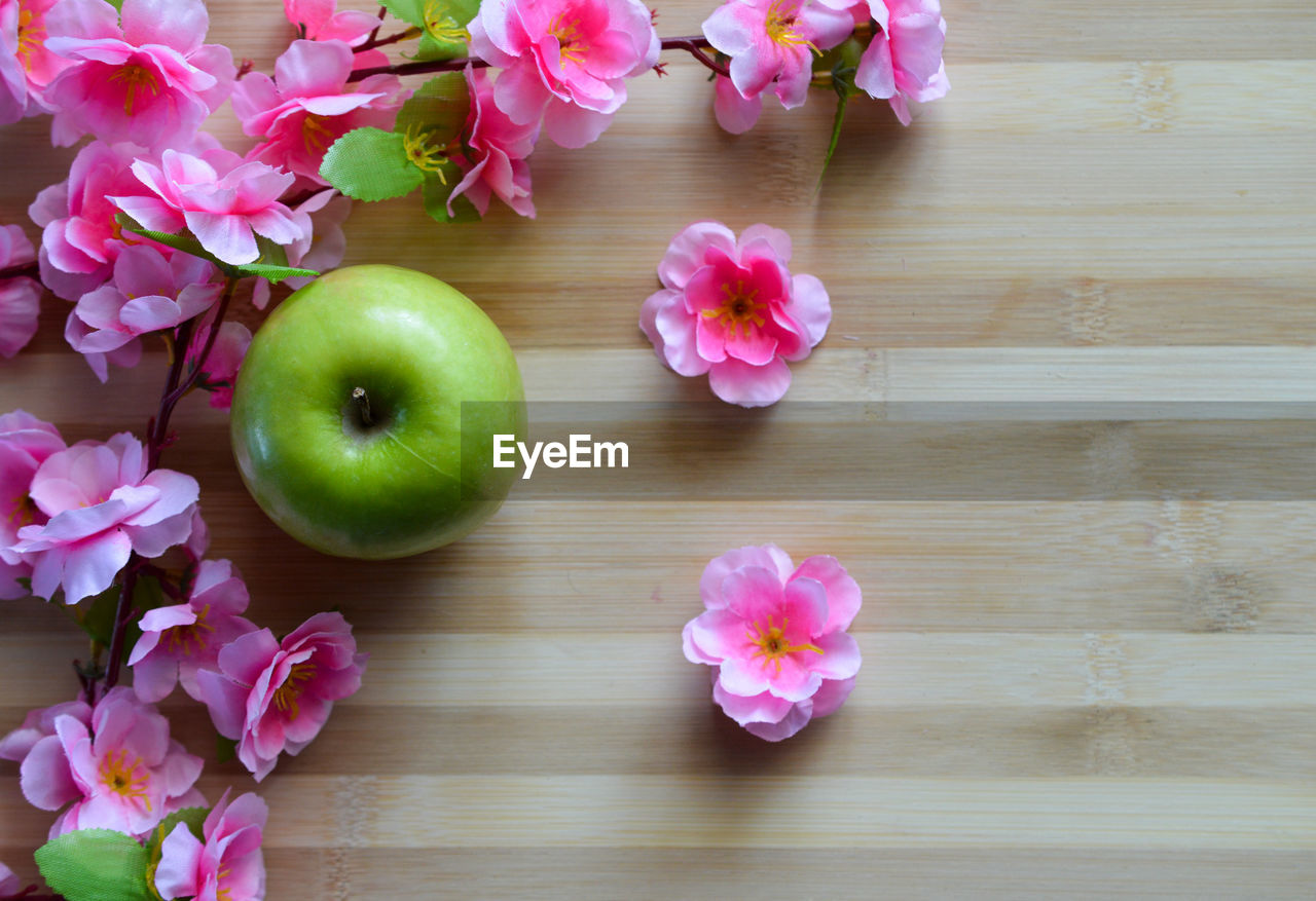 pink, freshness, flower, plant, flowering plant, beauty in nature, wood, nature, table, no people, food and drink, apple, indoors, food, still life, high angle view, close-up, directly above, apple - fruit, arrangement, wellbeing, fruit, petal, flower head, healthy eating, green, inflorescence