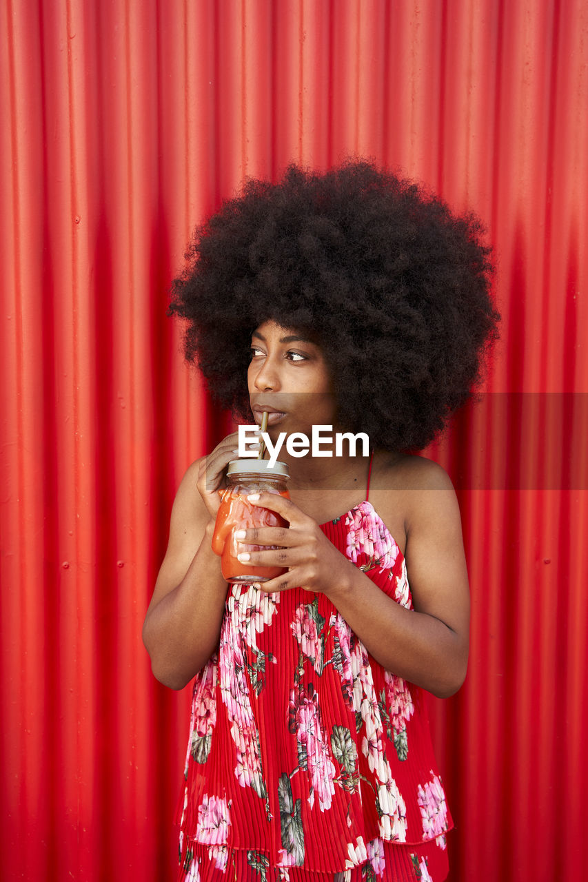 Woman drinking smoothie while standing in front of red wall