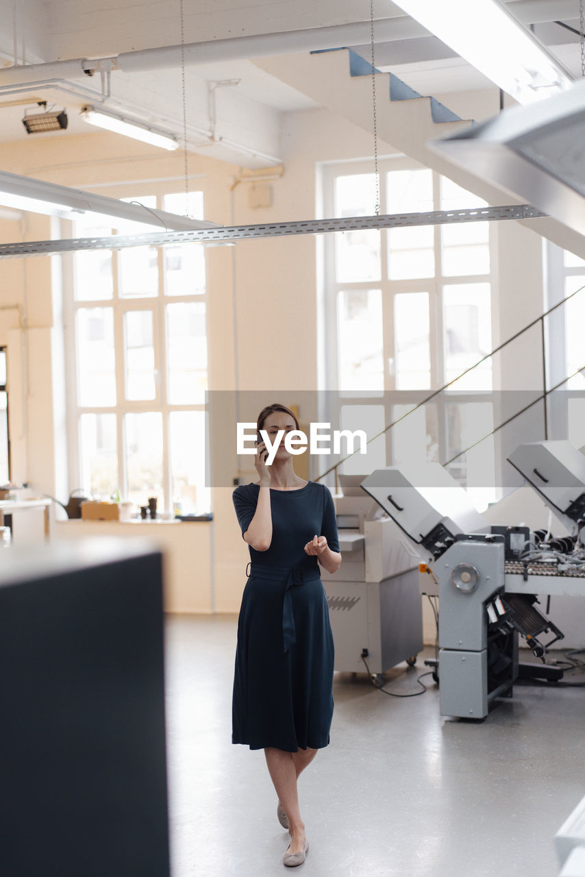 Businesswoman talking on mobile phone while walking in workshop