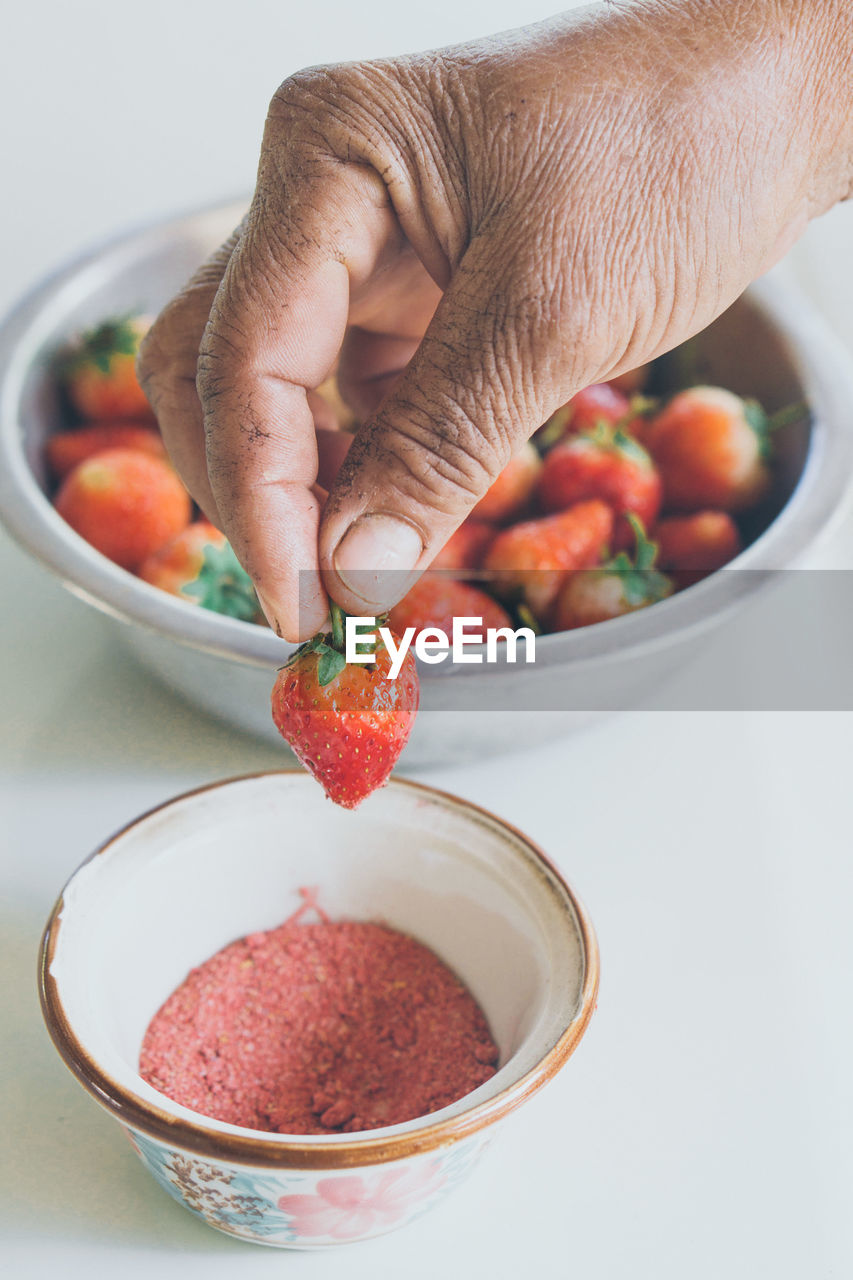 HIGH ANGLE VIEW OF HAND HOLDING BOWL WITH FRUITS