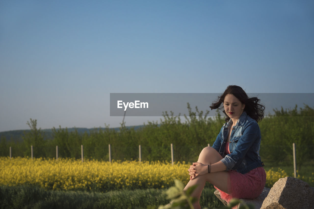 Woman sitting on field against clear sky