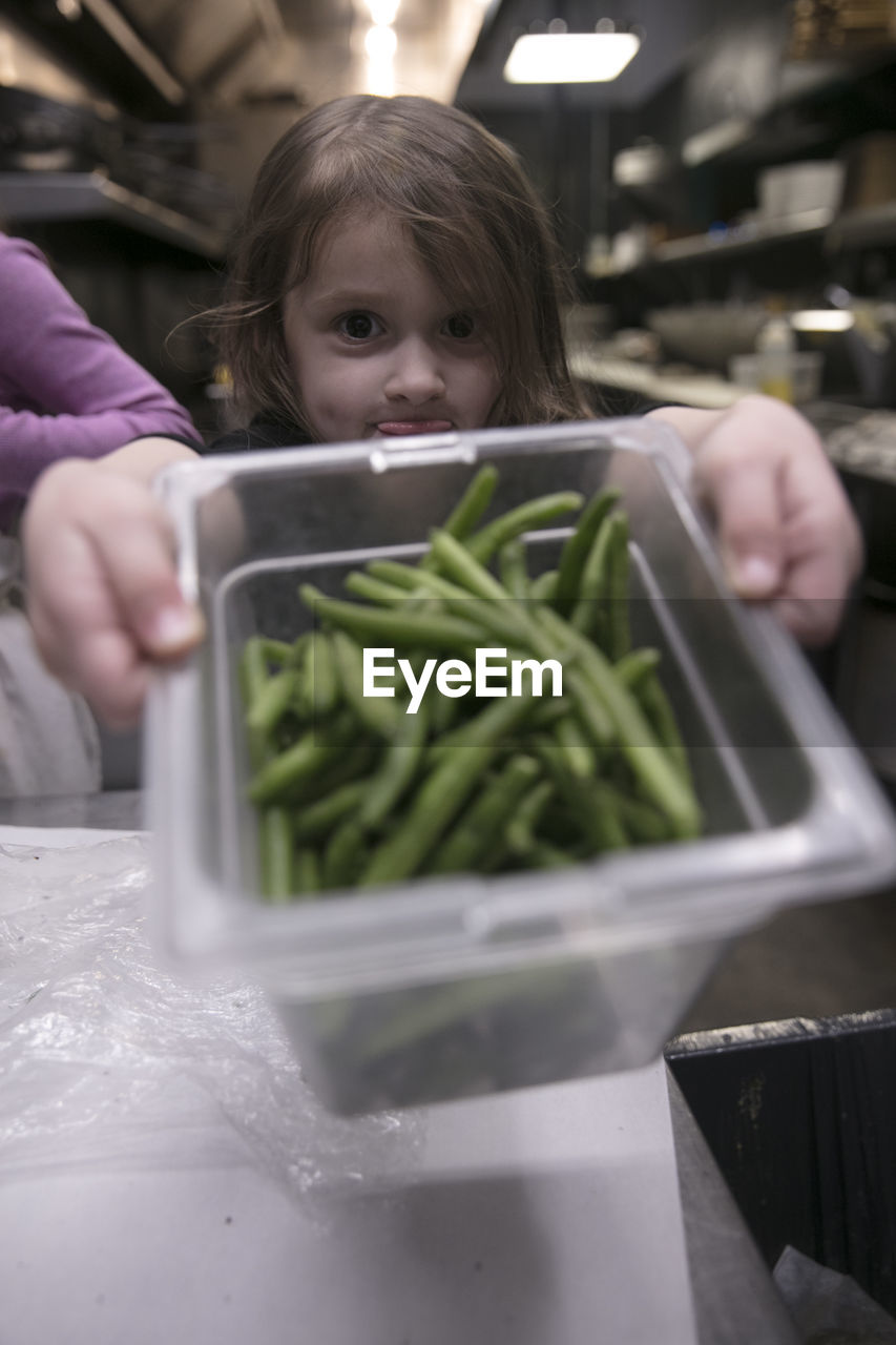 Girl holding green beans in container in kitchen