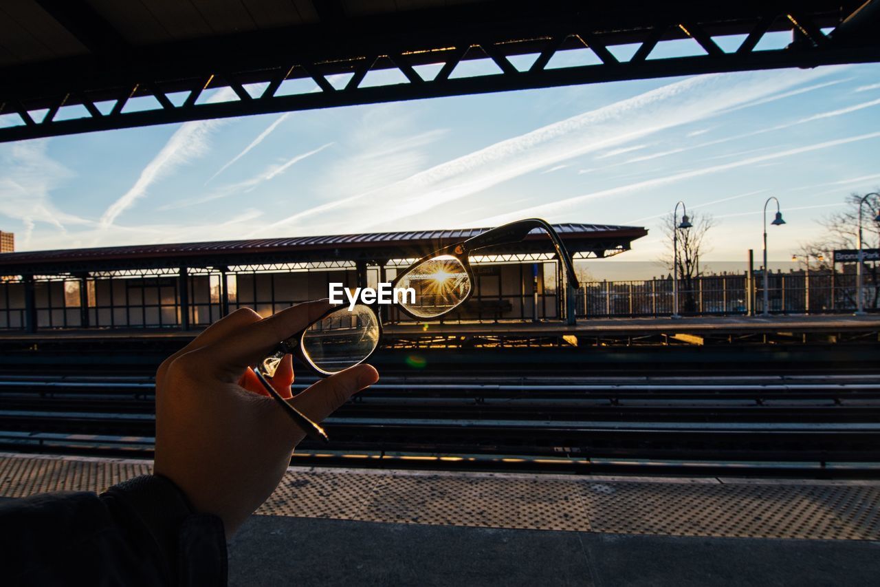 Cropped image of hand holding eyeglass at railroad station
