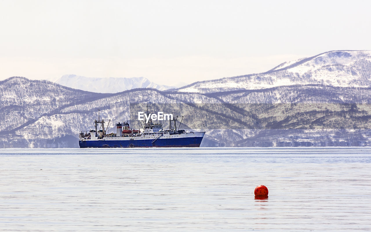 Large fishing vessel on the background of snow-covered hills and volcanoes 