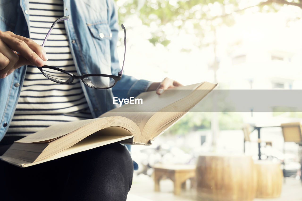 Midsection of woman with eyeglasses holding book