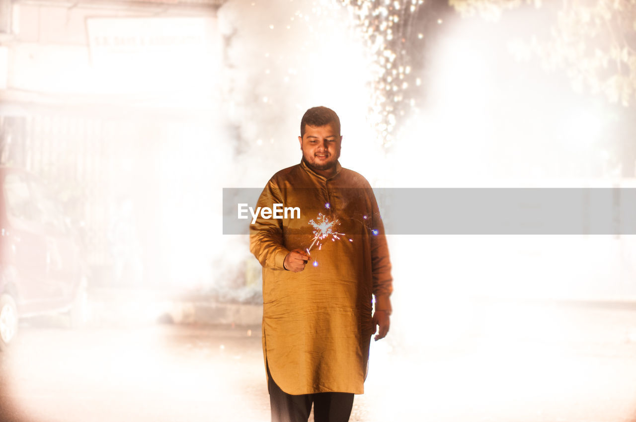 Man holding lit sparkler while standing at night during diwali