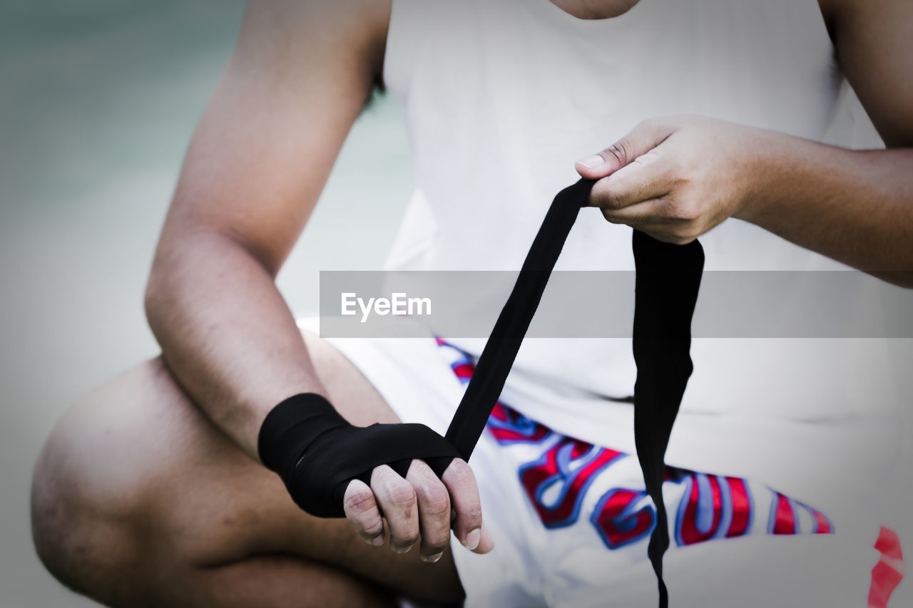 Midsection of boxer tying bandage while crouching on road